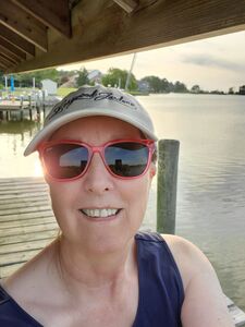 A woman in a hat and sunglasses sitting on a dock