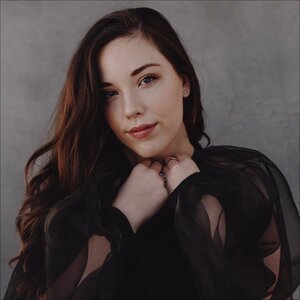 Woman with long dark hair in a sheer black top, softly smiling at the camera.