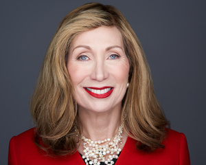 Franmarie Kennedy, author, smiling in a red jacket and layered pearl necklaces