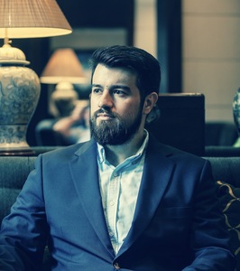 A three-quarter shot of Andrew P. Rowan taken at the Metropole Hotel in Hanoi, Vietnam. He is looking intently to the left of the photographer, with a composed expression. The background subtly reflects the hotel's historic ambiance.
