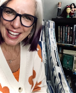 Close up of author sitting on chair with bookcase behind her.