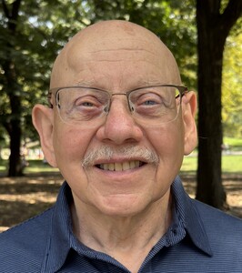 Bald, older man with glasses and a gray mustache with trees in the background