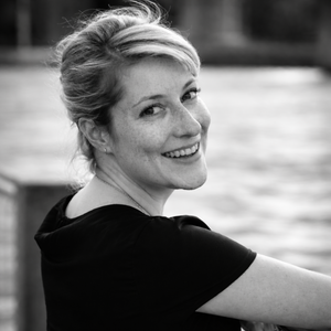 Black-and-white portrait of author Mariela Haack smiling at the camera beside the water.