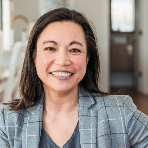 Photo of a smiling Asian American woman wearing a gray, plaid suit jacket and looking slightly to the right.