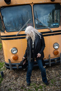 stina leicht standing in front of a vintage school bus once used as a tour bus by some random band