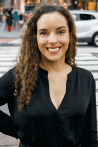 Kaitlyn Wells, with long curly hair, is standing outdoors and wearing a black top
