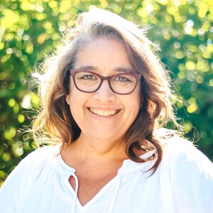 Photo of Jen Graybeal wearing a white shirt and standing in front of greenery. 