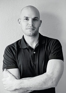 Author portrait: Black-and-white portrait of Thanos Panagopoulos standing with arms crossed, wearing a polo shirt.