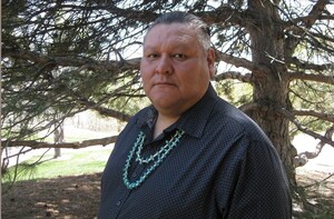 Image is the indigenous author posing in front of a pine tree.