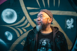 author photo of Khan Wong, standing in front of a graffitied wall