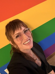 Lasara--a red haired, brown eyed. nonbinary white person--in glasses, a bandana and cap, and a coveralls.