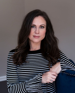 Woman in a black and white striped, long-sleeved top clasping hands as she leans against a navy chair