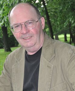 alt="Photo of author Richard H. Underwood sitting in park in the spring, wearing a tan jacket and black shirt."
