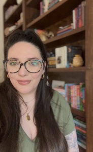 woman with long brown hair and glasses smiles in front of a bookshelf