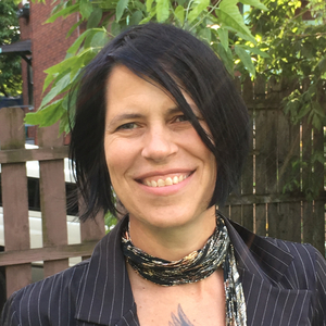 photo of smiling, white woman with dark brown hair and a sparkly scarf, with an outdoor backdrop.