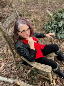 Ana K Wrenn sits in a wooden rocking chair in a wild area
