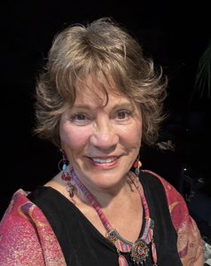 Smiling woman with short light brown hair, wearing a pink necklace.