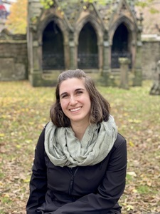 Brown-haired woman sitting in front of a stone arch, wearing a green scarf