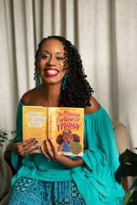Nicole D. Collier, a Black middle grade author, smiling while holding The Many Fortunes of Maya