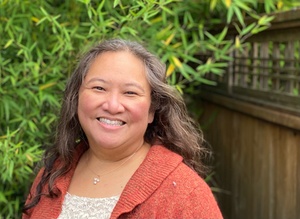 Asian American woman with wavy hair and orange sweater