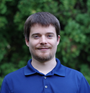 A photo portrait of a man with short brown hair and wearing a blue polo shirt in front of a green tree background.