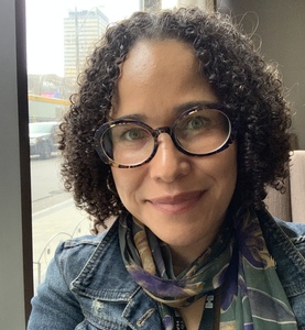 author with curly hair wearing glasses and denim jacket