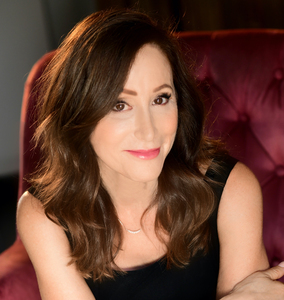 Headshot of a smart, beautiful brown-eyed woman in a sleeveless black dress with arms crossed