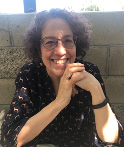 Woman with curly dark hair and glasses smiling into the sunlight.