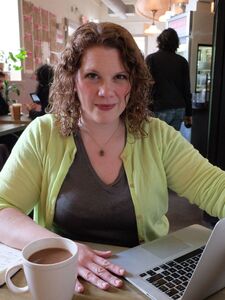 Red haired white woman sits in front of a computer with a cup of coffee by her hand