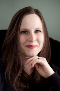 A white woman with brown hair looks at the camera with her hand under her chin