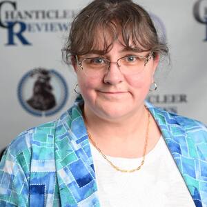 A photograph of dark haired woman standing in front of a step and repeat backdrop reading Chanticleer Reviews