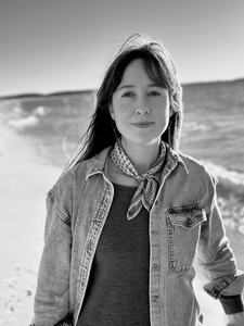 A black and white picture of me on the shore of Lake Michigan. I'm a white woman with long hair, wearing a denim shirt with a small keffiyeh tied around my neck.