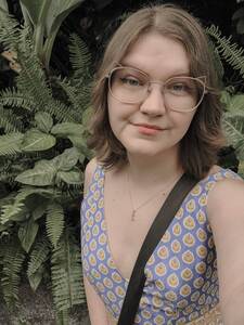 Woman in vintage 70s dress smiling in front of green shrubbery