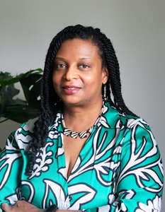 Yvette is wearing a graphic green and white blouse. Her arms are crossed and she is smiling.
