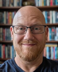 Brandon Reynolds headshot set against a blurred background of shelves filled with books.