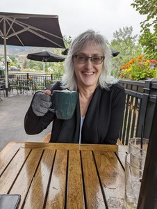 A woman sitting at an outdoor cafe holding up a mug of hot chocolate.