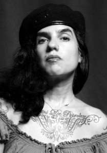 Queer, Cuban, femme artist with black hat, black hair, black eyebrows, and brown eyes in black and white 