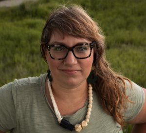 A plus size brunette woman standing in a field smiles demurely at the camera. ;-)