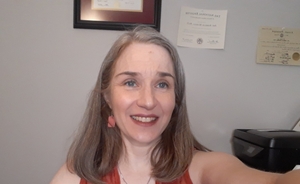 Middle-aged woman with auburn hair and blue eyes in orange dress facing forward to camera