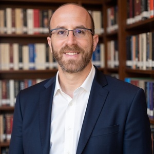 Man in blue blazer with white shirt in front of bookshelf