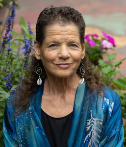 middle-aged woman with brown hair and silver earrings, looking directly into camera with garden flowers behind her