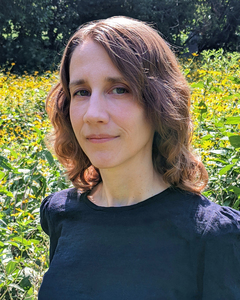 Writer Kate Blakinger wearing a black shirt standing in front of a field of yellow wildflowers