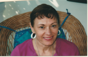 Smiling woman in wicker chair; brown hair wearing magenta blouse 