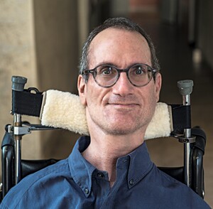 A middle-aged white guy with a crooked half-smile, wearing glasses and a dark-blue button shirt.