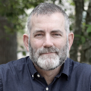 Writer Todd Warner, traditionally male in appearance, bearded, staring into the camera wearing a blue button-down shirt.