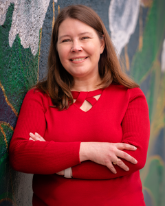 photo of Sally Kilpatrick wearing a red sweater and leaning up against a wall