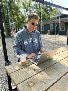 Guy who thinks he’s cool sits at a picnic table pretending to write on a laptop but he is really just posing for a picture