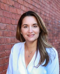 Female author wearing a white shirt with a brick wall in the background.