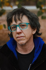Heatshot of a masculine person wearing blue framed glasses and a black shirt