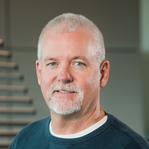Caucasian man with close-cropped gray hair, wearing a green shirt